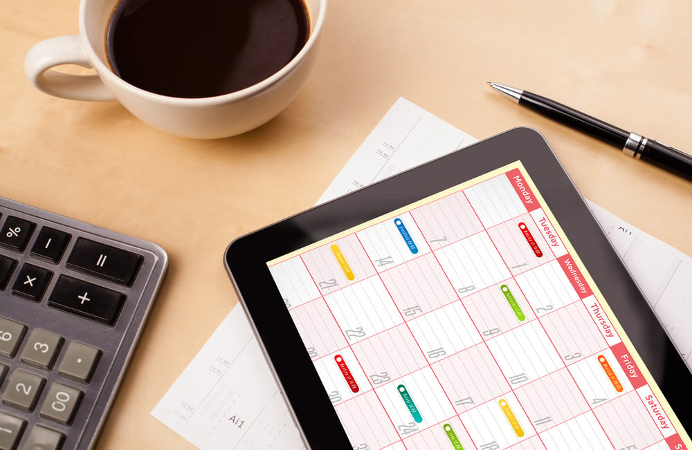 Workplace with tablet pc showing calendar and a cup of coffee on a wooden work table close-up